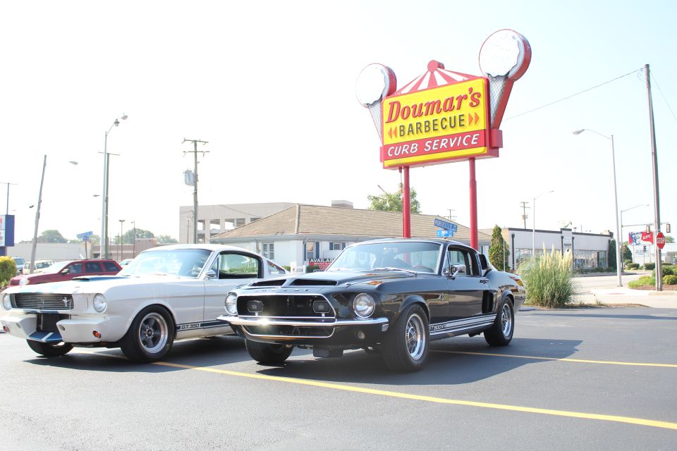 Black 1967 Ford Mustang GT500 and a white 1965 Ford Mustang parked outside Doumar's Barbecue