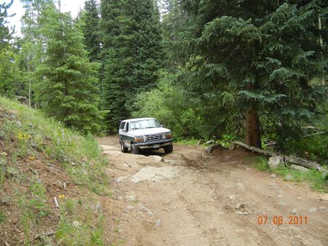 1996 Ford Bronco - SUV navigates a challenging, rocky path through a dense forest.
