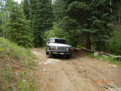 1996 Ford Bronco - A Ford Bronco navigates a rough, wooded trail, kicking up dust on the path ahead.
