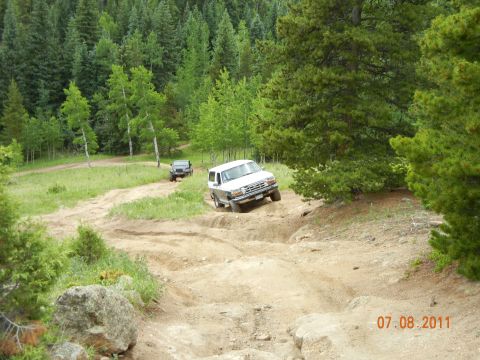 1996 Ford Bronco - Two SUVs navigate a challenging off-road trail through a wooded area.