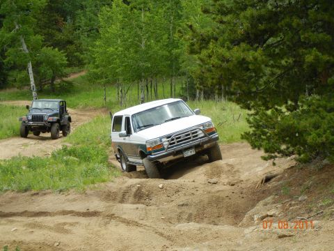 1996 Ford Bronco - A 1996 Ford Bronco navigates a challenging dirt trail, with another Jeep visible in the background.