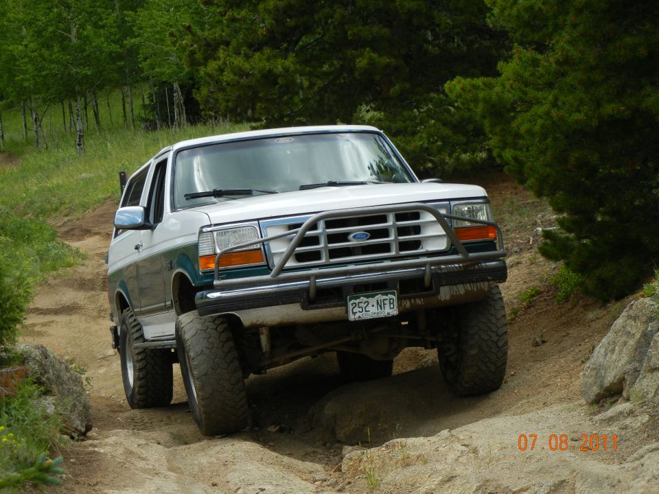 White and green Ford Bronco on a dirt trail, front view, with a brush guard