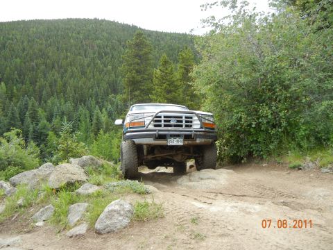 1996 Ford Bronco - This Ford truck is navigating a rocky off-road trail with dense forest in the background.