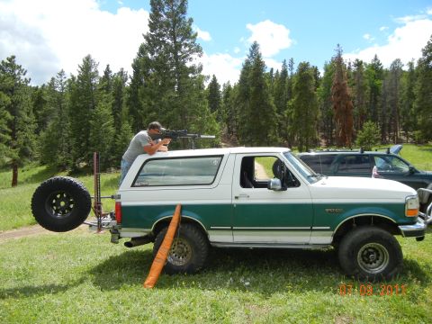 1996 Ford Bronco - A man aims a rifle from the roof of a 1996 Ford Bronco, with another vehicle visible in the background.