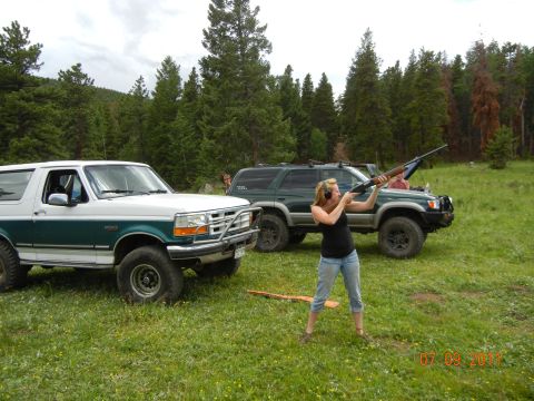 1996 Ford Bronco - Two SUVs are parked in a grassy, wooded area, with a woman aiming a shotgun.