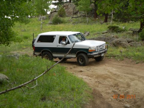1996 Ford Bronco - A white and green 1996 Ford Bronco navigates a dirt path in a wooded, rocky area.