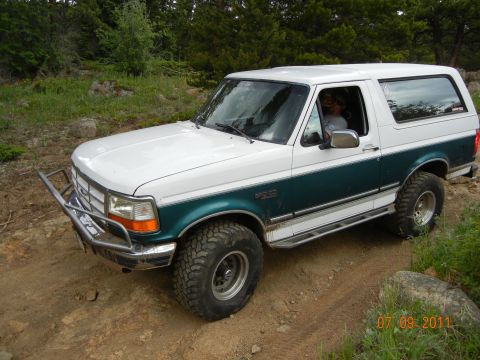 1996 Ford Bronco - This 1996 Ford Bronco is shown off-roading on a dirt path with trees in the background.