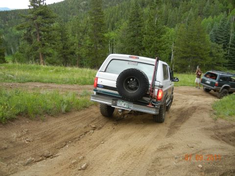 1996 Ford Bronco - Two SUVs navigate a dirt trail through a wooded area.