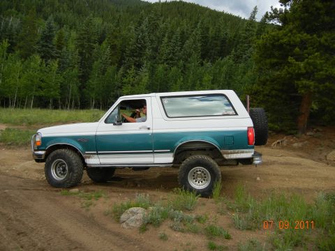 1996 Ford Bronco - This 1996 Ford Bronco is captured in a side profile as it navigates a dirt road through a wooded area.