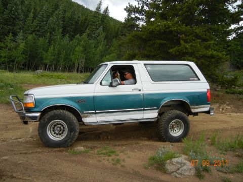1996 Ford Bronco - 1996 Ford Bronco driving on a dirt trail in a wooded area.