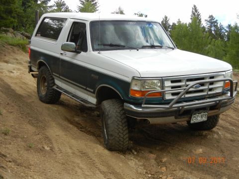 1996 Ford Bronco - A 1996 Ford Bronco is shown on a dirt path with trees in the background.