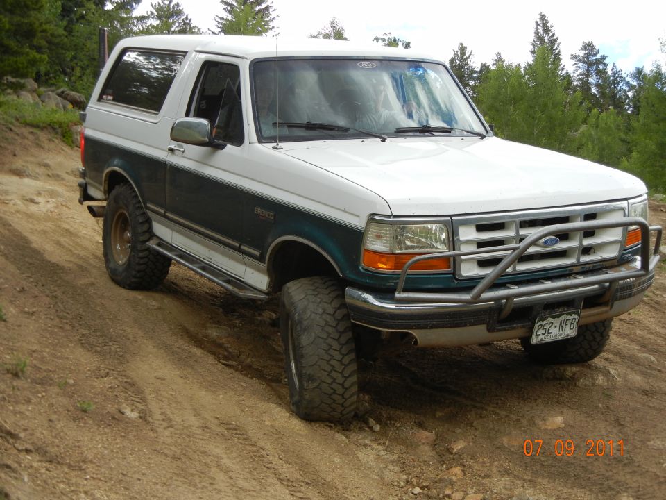 White and dark green 1996 Ford Bronco with bull bar and off-road tires on dirt road