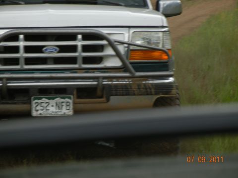 1996 Ford Bronco - This Ford truck, likely from the early 90s, is equipped with a heavy-duty brush guard and appears to be on a dirt road.