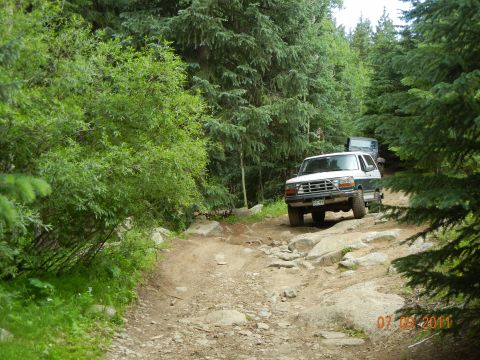 1996 Ford Bronco - A 1996 Ford Bronco navigates a challenging, wooded off-road path, followed by another vehicle.