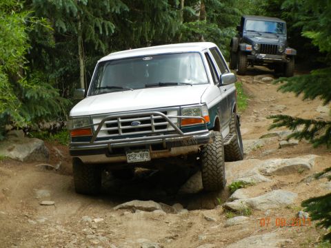 1996 Ford Bronco - A white and teal Ford Bronco navigates a challenging rocky off-road trail, with a Jeep following behind.
