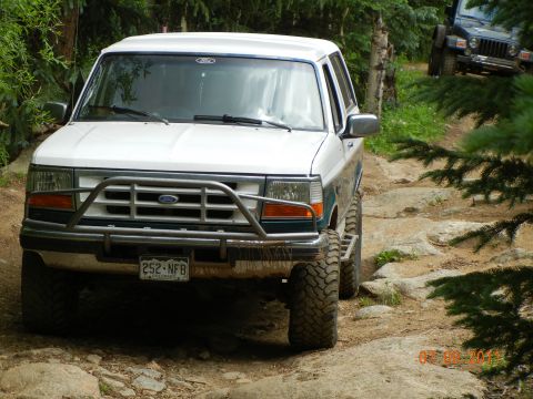 1996 Ford Bronco - White Ford Bronco navigates a rocky off-road trail with another vehicle behind it.