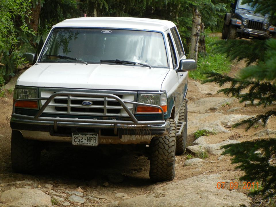 White Ford Bronco with aftermarket bumper on rocky trail, another Jeep visible in background