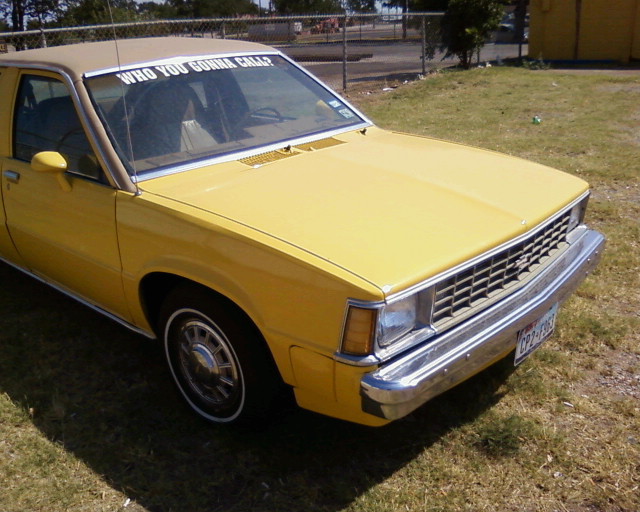 Yellow 1981 Chevrolet Citation with a tan roof and a banner reading "WHO YOU GONNA CALL?" on the windshield