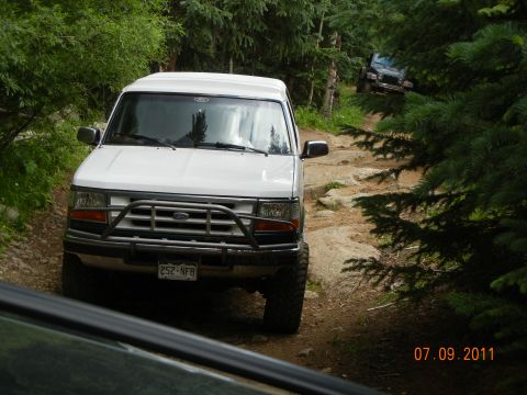 1996 Ford Bronco - A white Ford Bronco navigates a challenging, rocky path through a dense forest.