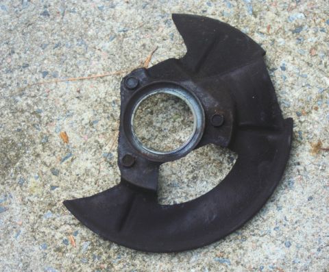 1980 Ford Mustang - A worn brake dust shield lies on a concrete surface, showing signs of rust and age.