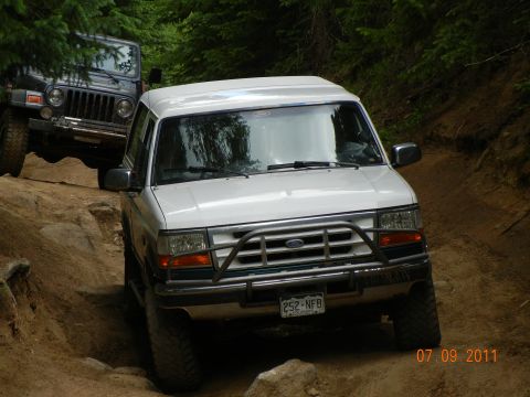 1996 Ford Bronco - Two off-road vehicles, a 1996 Ford Bronco and a Jeep Wrangler, navigate a challenging dirt path.