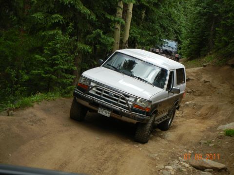 1996 Ford Bronco - A white 1996 Ford Bronco navigates a rocky dirt trail, with another vehicle following behind.