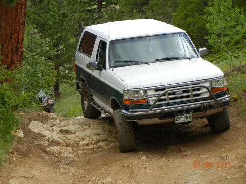 1996 Ford Bronco - A 1996 Ford Bronco navigates a challenging off-road path with another vehicle following.