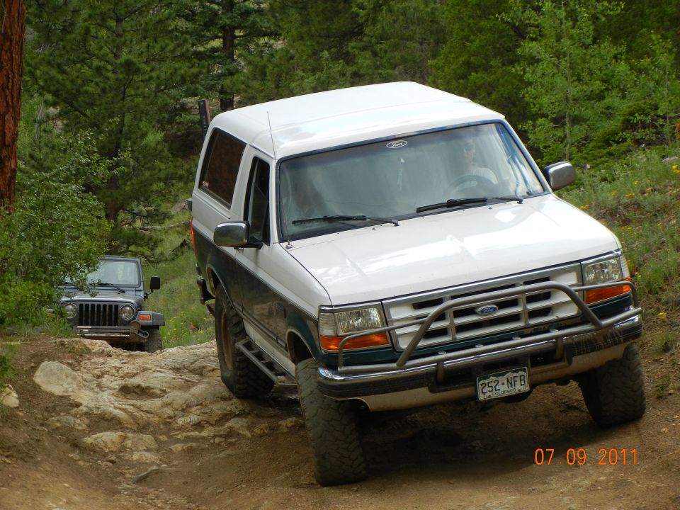 White and green 1996 Ford Bronco with brush guard on rocky trail, Jeep behind