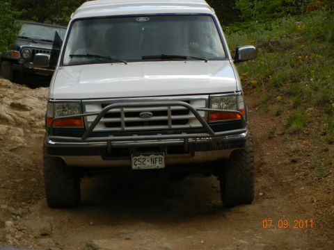 1996 Ford Bronco - 1996 Ford Bronco driving on an off-road trail, with another vehicle visible behind it.