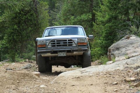 1996 Ford Bronco - A Ford Bronco navigates a rocky, off-road trail surrounded by dense forest.