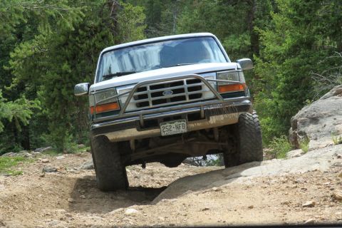 1996 Ford Bronco - A white Ford Bronco navigates a rocky, off-road trail.
