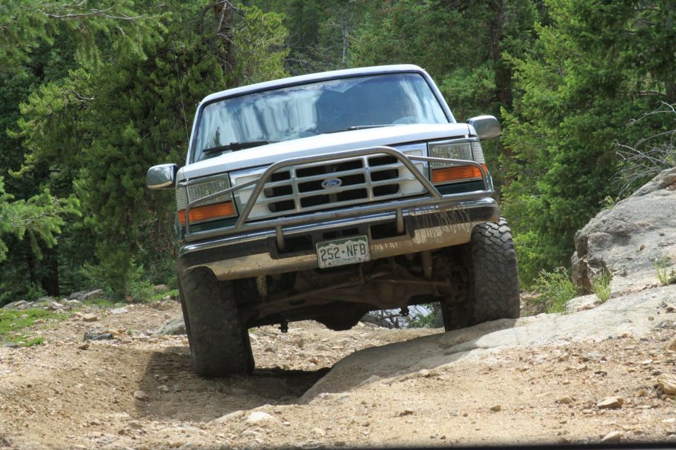 White Ford Bronco on a dirt trail, front view, with a brush guard and off-road tires