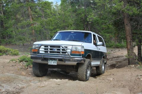 1996 Ford Bronco - A two-tone Ford Bronco navigates a wooded off-road path.