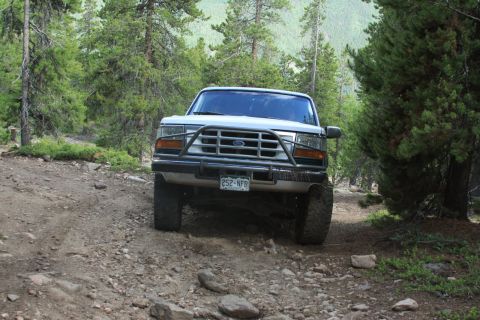 1996 Ford Bronco - A white Ford Bronco navigates a rough, wooded trail.
