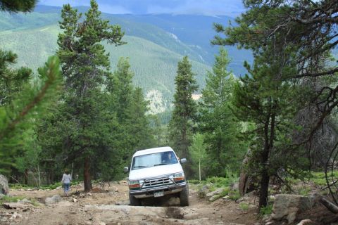 1996 Ford Bronco - A white 1992 Ford Bronco navigates a challenging rocky path through a mountainous, forested landscape.