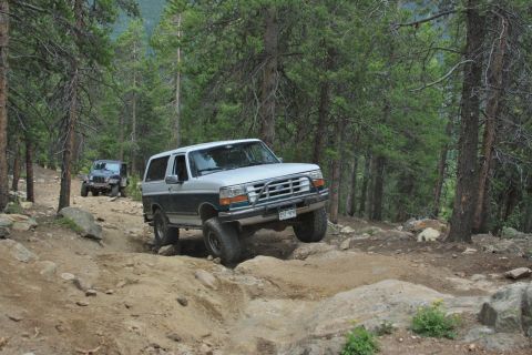 1996 Ford Bronco - A two-tone 1996 Ford Bronco navigates a challenging rocky trail, with another SUV following in the background.