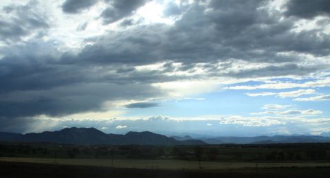1996 Ford Bronco - A dramatic sky with heavy clouds looms over a mountain range and a rural landscape.