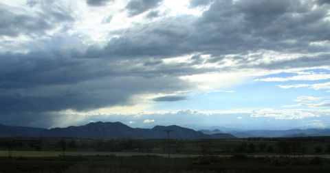 1996 Ford Bronco - A dramatic sky with dark clouds looms over a distant mountain range and rural landscape, with a website logo in the corner.