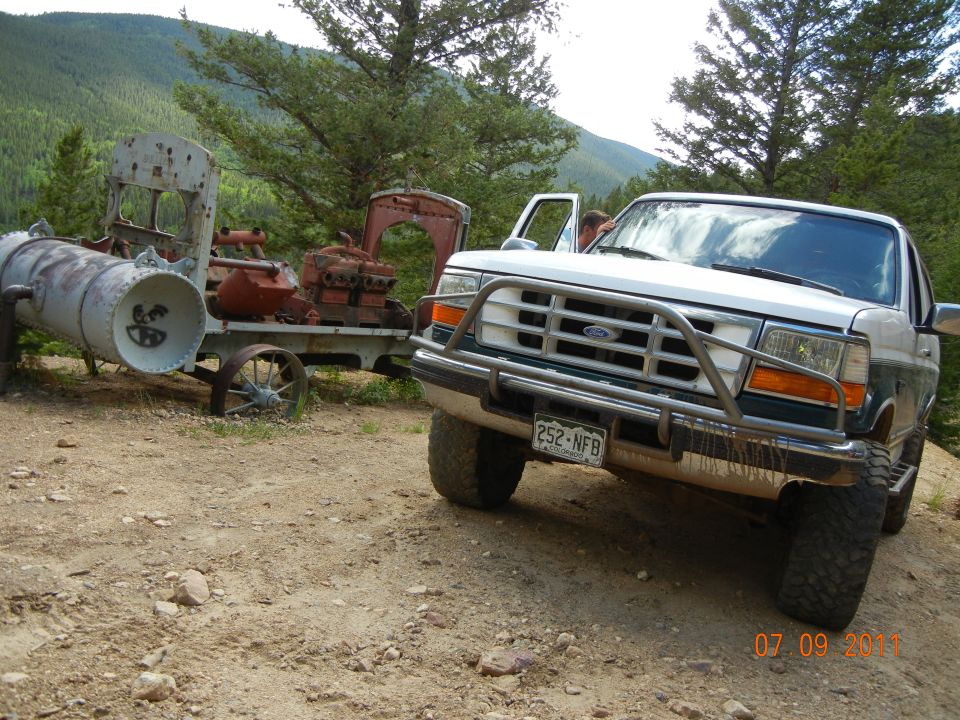 1996 Ford Bronco parked next to rusty industrial machinery on a dirt road
