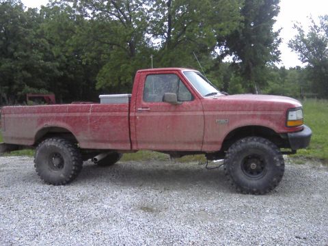 1995 Ford F-150 - This red 1995 Ford F-150 pickup truck is shown in profile, a lifted suspension and oversized off-road tires.