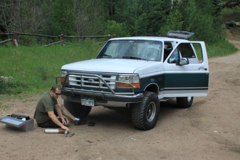 1996 Ford Bronco - A man is working on a 1996 Ford Bronco parked on a dirt road with trees in the background.