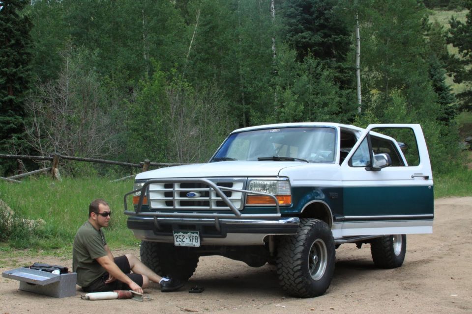 White and teal Ford Bronco with aftermarket bumper and lifted suspension sits on a dirt road