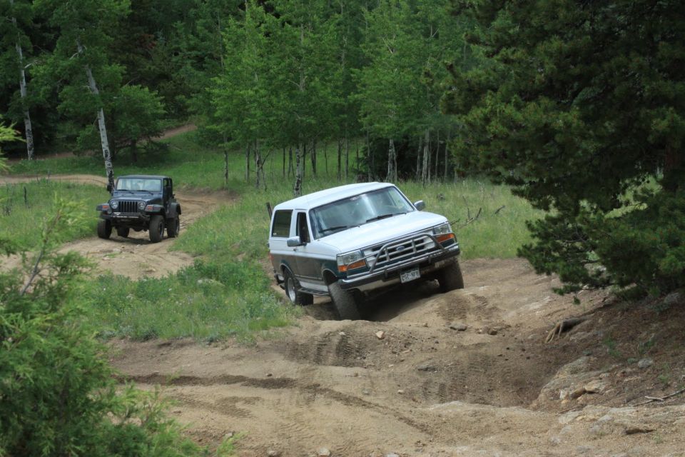 White and gray Ford Bronco on a dirt trail, angled right, with a black Jeep in the background