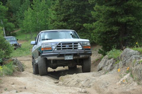 1996 Ford Bronco - 1996 Ford Bronco navigates a challenging off-road path, with another vehicle visible ahead.