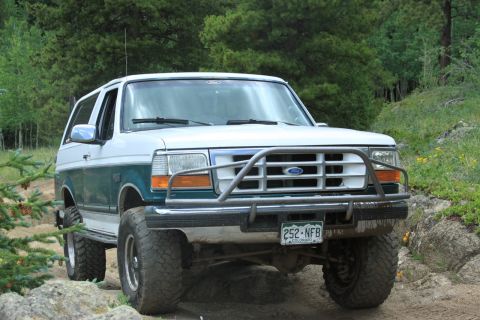 1996 Ford Bronco - This Ford Bronco is equipped with a brush guard and is driving on a dirt path with trees in the background.