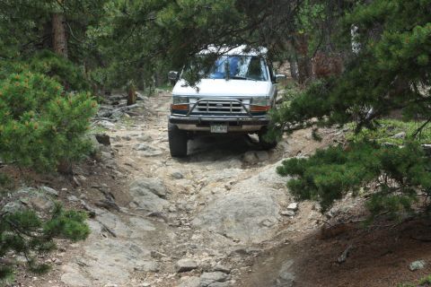 1996 Ford Bronco - White 1996 Ford Bronco navigates a challenging rocky path in a wooded area.