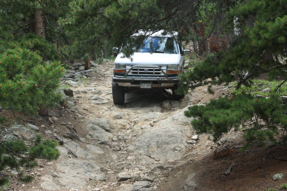 1996 Ford Bronco driving on a rocky trail surrounded by trees