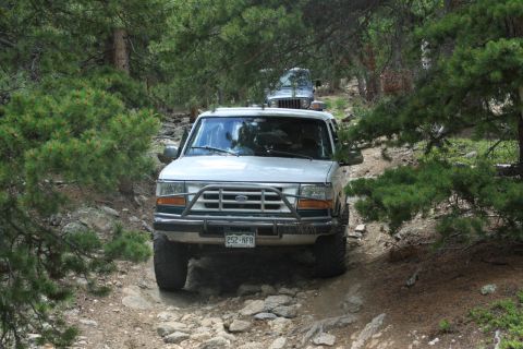 1996 Ford Bronco - A 1996 Ford Bronco navigates a rough, forested path, with another vehicle following behind.