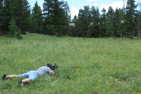 1996 Ford Bronco - A person lies in a grassy field, aiming a rifle towards the trees.