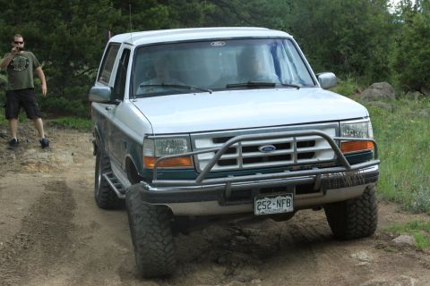 1996 Ford Bronco - A white Ford Bronco with a brush guard is parked on a dirt road, with a man standing nearby.
